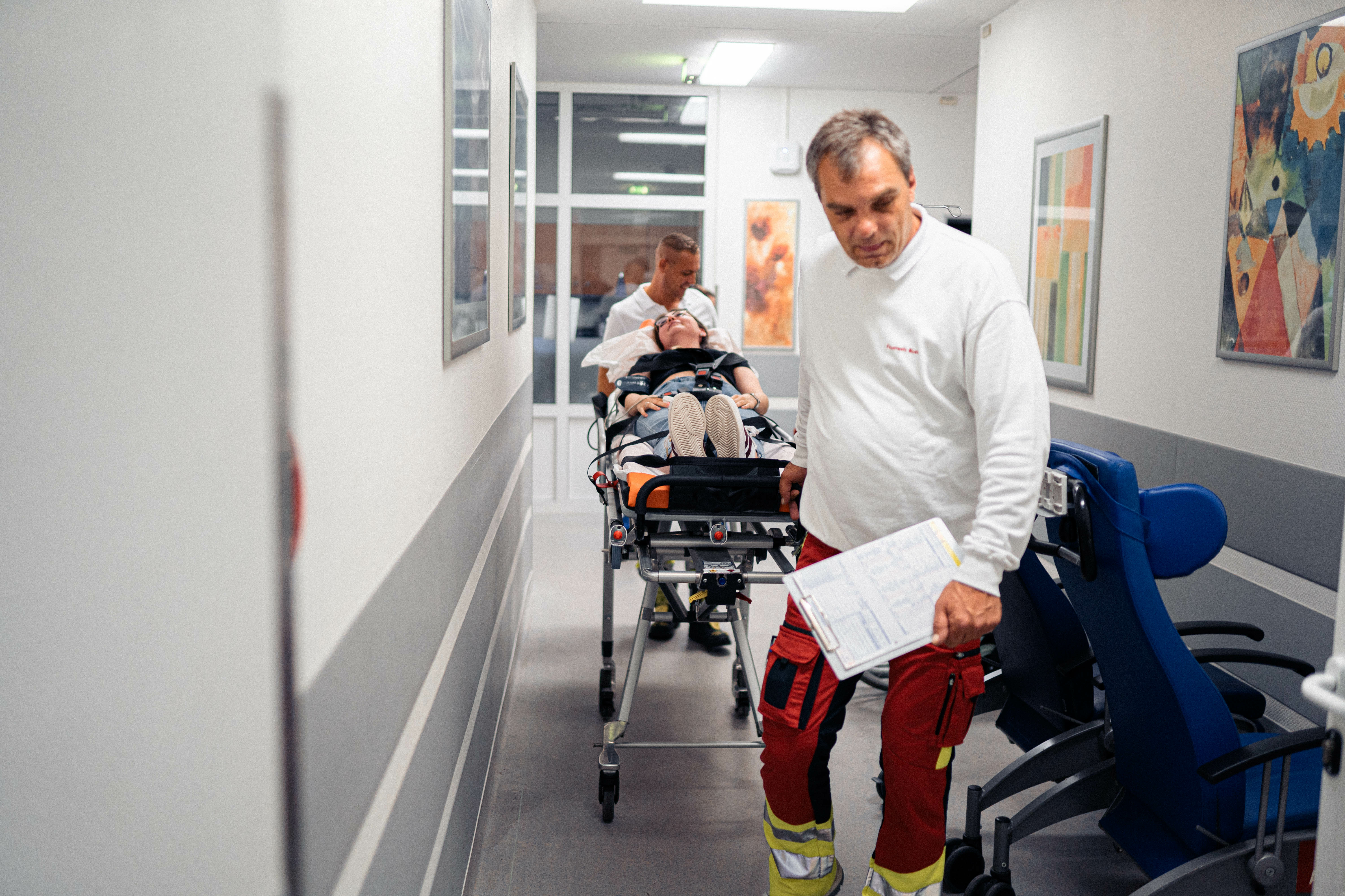 Eine Patientin liegt auf einer Trage und wird von zwei Notfallsanitätern in die Räumlichkeiten der Zentralen Notaufnahme gebracht. 